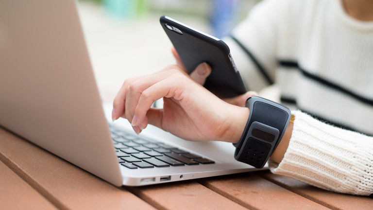 person wearing smart watch, working on laptop and holding smart phone