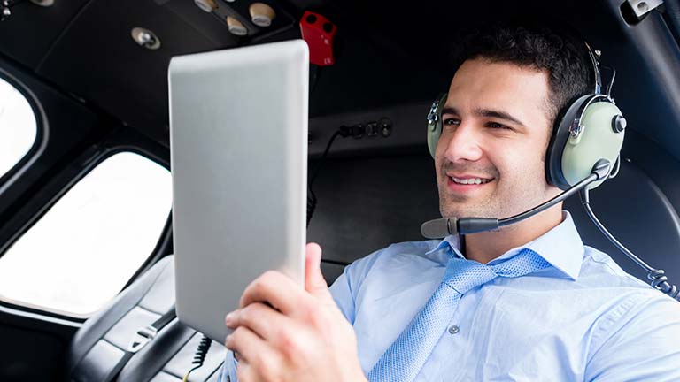 Man sitting in an airplane listening to headphones and looking at a tablet